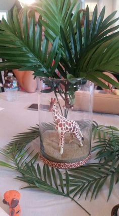 a small giraffe in a glass vase on top of a table with palm leaves