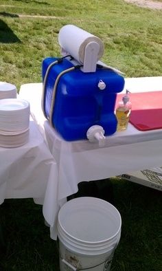 a blue cooler sitting on top of a white table covered in plates and cups next to a bucket