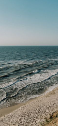 an empty beach next to the ocean with waves coming in from the water and sand