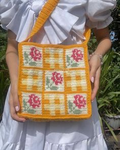 a woman is holding a crocheted purse in front of some plants and bushes