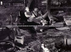 black and white photo of two men sitting on an old couch in front of a fire hydrant