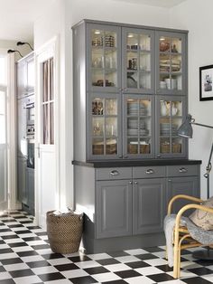 a kitchen with black and white checkered flooring, glass fronted cabinets and chairs