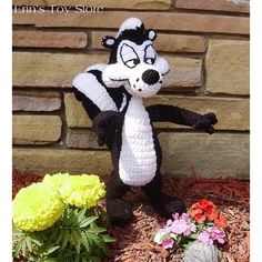 a crocheted skunk is standing in front of a brick wall and flowers