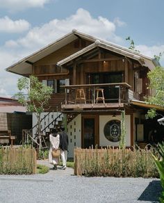 two people standing in front of a house with a wooden fence and green plants on the side