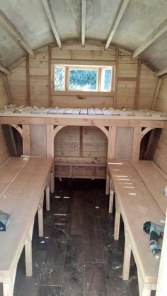 the inside of a small wooden building with benches and tables on each side, in front of a window