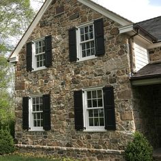 an old stone house with black shutters on the windows and white trim around the windows