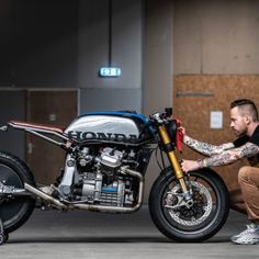 a man kneeling down next to a motorcycle in a garage with his hand on the wheel