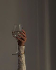 a woman's hand holding a wine glass in front of her face with glitter on it