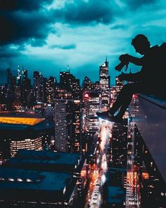 a man sitting on top of a tall building next to a cityscape at night