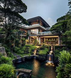 the house is surrounded by lush green trees and water features a waterfall that flows into the pool