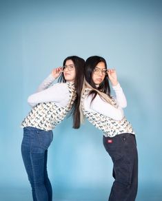 two women are standing in front of a blue background and one is holding her hair back