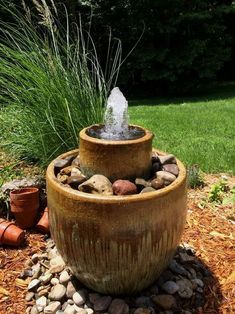 an outdoor fountain with rocks and water in the center, surrounded by plants and grass