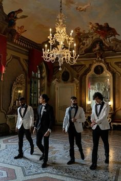 four men in tuxedos are standing on the floor with chandelier above them