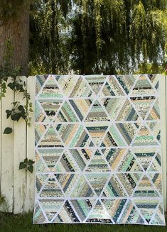 a quilt hanging on the side of a white fence next to a tree and grass