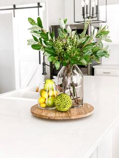 a glass vase filled with green leaves and fruit on top of a white countertop