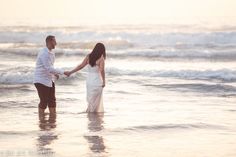 a man and woman holding hands while standing in the water at sunset on the beach