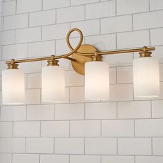 a bathroom light fixture with five lights on it's side against a white brick wall