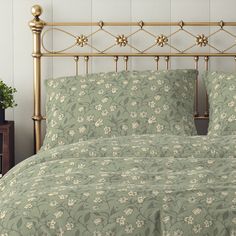 a bed with green and white floral bedspread on top of it next to a night stand