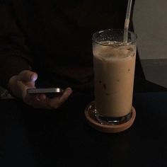 a person holding a cell phone next to a drink on a table with a straw in it