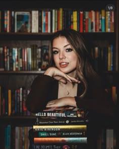 a woman leaning on a stack of books in front of a book shelf with many books