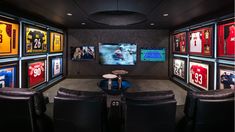 a room filled with black leather chairs and framed pictures on the wall behind two large screen televisions