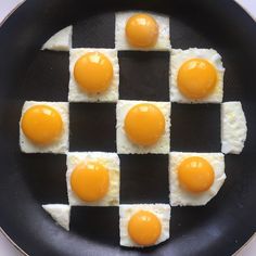 four eggs are arranged in the shape of squares on a black pan with white rice