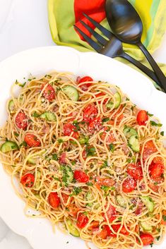 a plate of pasta with tomatoes and zucchini on it next to a fork