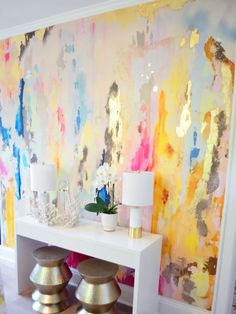 a white table topped with two stools next to a wall covered in colorful paint