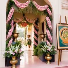 an archway decorated with pink flowers and greenery in front of a painting on the wall