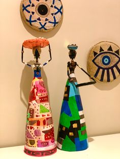 two colorful vases sitting next to each other on a table with artwork behind them