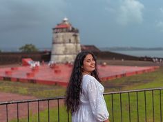 a woman standing next to a fence with a lighthouse in the background