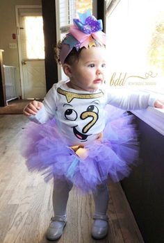 a baby girl wearing a purple tutu with a face on it's shirt