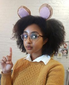 a woman with glasses and bunny ears on her head making the peace sign while sitting in an office