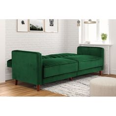 a green couch sitting on top of a wooden floor next to a white brick wall