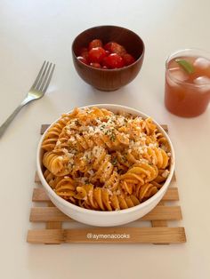 a white bowl filled with pasta and garnished with parmesan cheese next to a drink