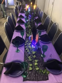 the table is set with purple and green place mats, black napkins, silverware, and candles