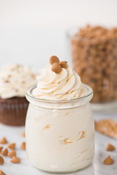 a cupcake in a glass jar with frosting and nuts on the table next to it