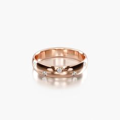 an 18k rose gold wedding ring with three diamonds on the inside and outside, set against a plain white background