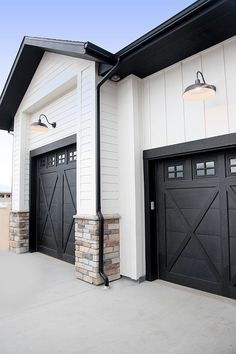 two black garage doors in front of a white house with an attached porch and brick pillars