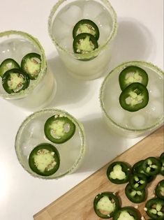 four glasses filled with green peppers sitting on top of a table next to a cutting board