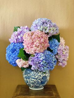 a blue and white vase filled with purple and pink flowers on top of a wooden table