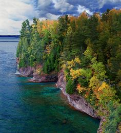 an aerial view of the water and trees in fall colors, along with dark clouds