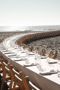 a long table is set with empty wine glasses and place settings for dinner on the beach