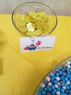 a bowl filled with blue and white candy next to a plate full of gold coins