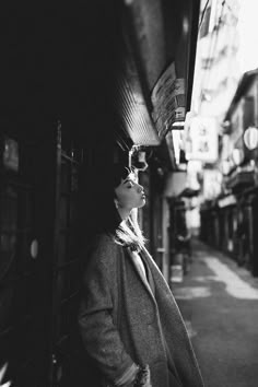 a woman standing on the side of a street next to a building and looking up