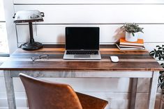 a laptop computer sitting on top of a wooden desk next to a chair and potted plant