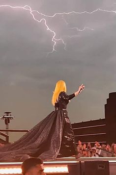 lady in black dress standing on stage with lightning behind her