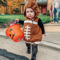 a small child in a costume holding a bucket and wearing a football helmet on the street