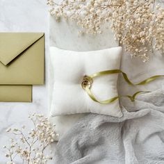 a white pillow with a ring on it next to some flowers and an envelope in the background