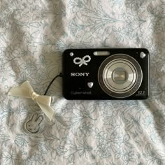 a black camera sitting on top of a bed next to a white ribbon and key